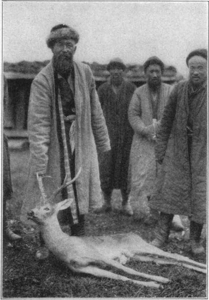 Several men stood around the body of a deer. One man is holding the deer's antler.