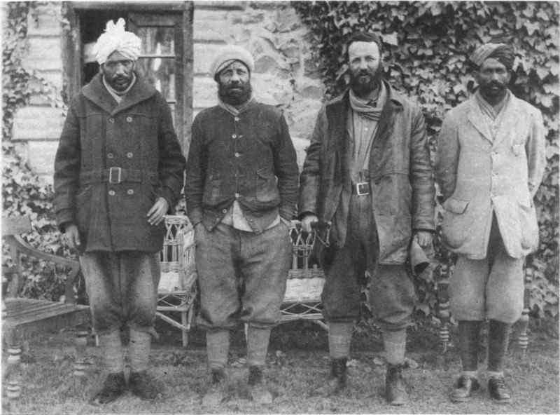 Four men in a row, facing the camera, in front of an ivy covered building.